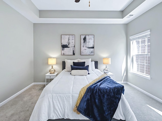 carpeted bedroom featuring a tray ceiling, visible vents, and baseboards