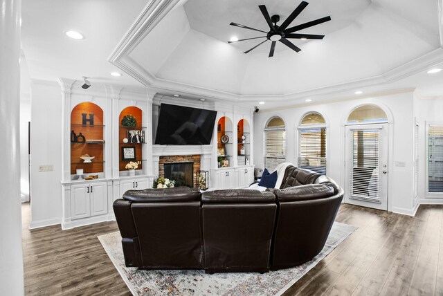 living room with a fireplace, wood finished floors, built in features, a raised ceiling, and crown molding