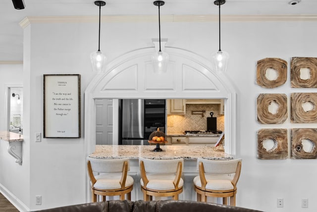 kitchen with crown molding, a breakfast bar area, backsplash, appliances with stainless steel finishes, and light stone countertops