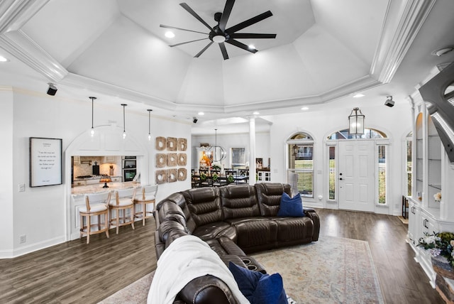 living area featuring high vaulted ceiling, ceiling fan with notable chandelier, wood finished floors, ornamental molding, and decorative columns