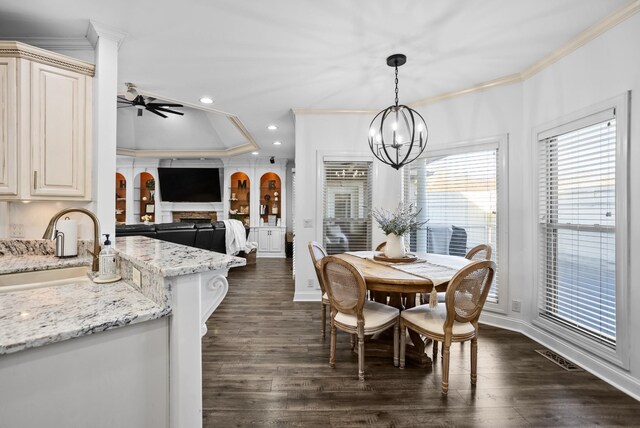 dining space with a fireplace, ornamental molding, dark wood finished floors, and ceiling fan with notable chandelier