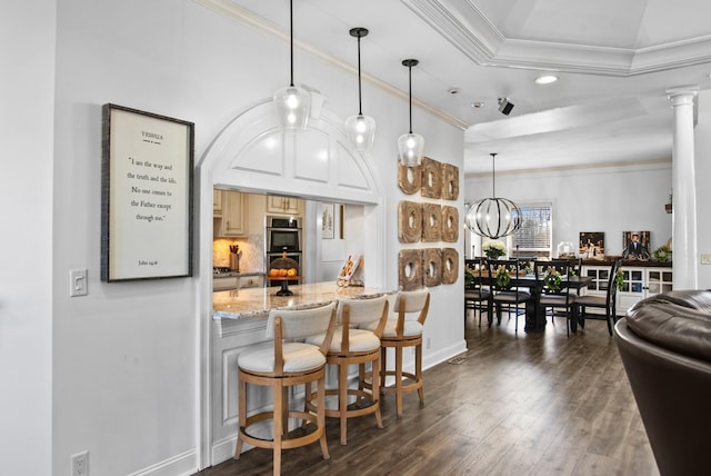 kitchen featuring ornate columns, ornamental molding, dark wood finished floors, and stainless steel double oven