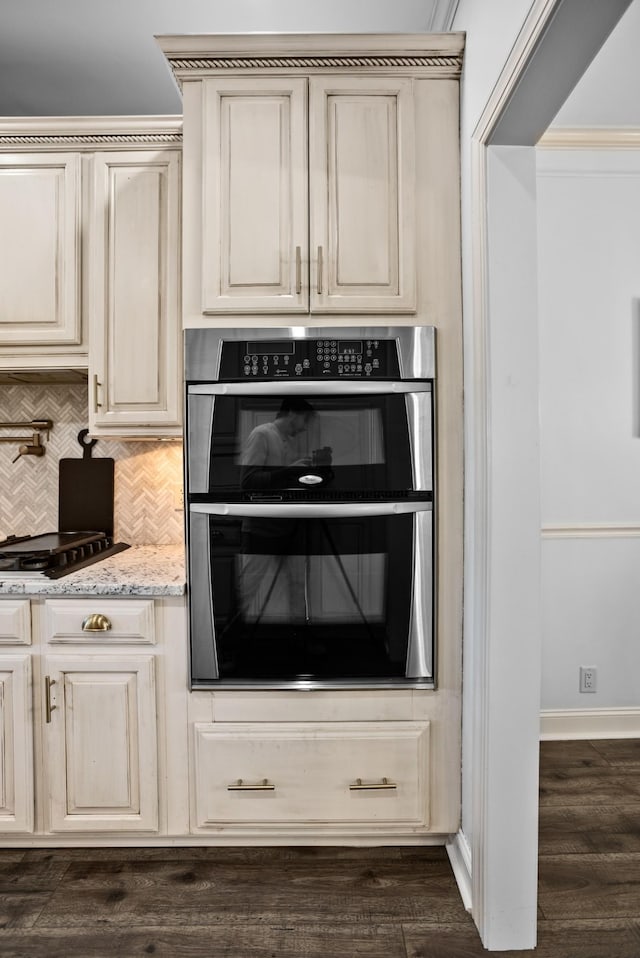 kitchen featuring tasteful backsplash, dark wood-type flooring, cream cabinets, stainless steel double oven, and black cooktop