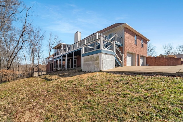 back of property featuring brick siding, a chimney, concrete driveway, a lawn, and an attached garage