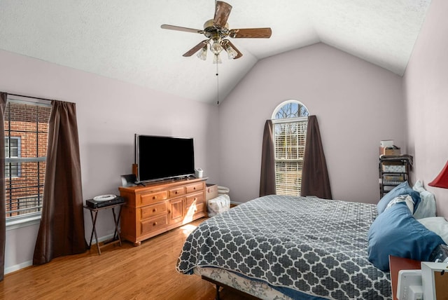 bedroom featuring light wood-style floors, a ceiling fan, vaulted ceiling, a textured ceiling, and baseboards