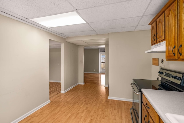 kitchen with baseboards, light wood-style flooring, brown cabinets, under cabinet range hood, and stainless steel range with electric stovetop