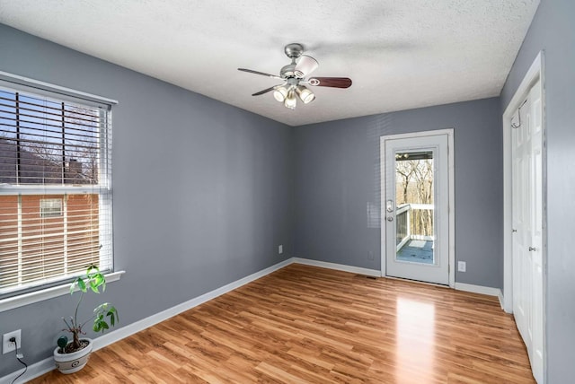 empty room with ceiling fan, light wood finished floors, a textured ceiling, and baseboards