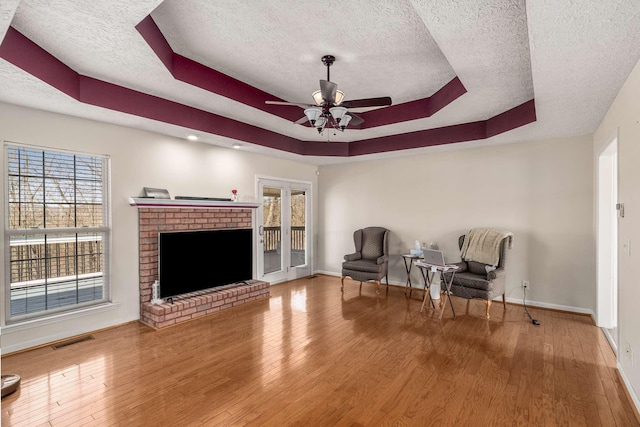 living area with a tray ceiling, a brick fireplace, wood finished floors, and visible vents