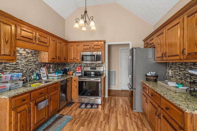 kitchen featuring visible vents, brown cabinetry, appliances with stainless steel finishes, light wood-type flooring, and a sink