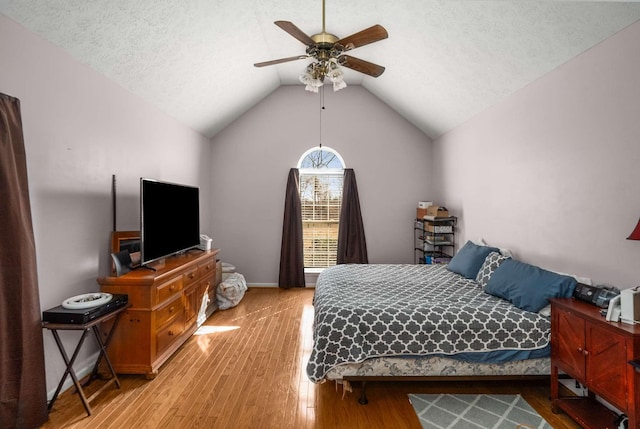 bedroom featuring vaulted ceiling, a textured ceiling, light wood-type flooring, and a ceiling fan