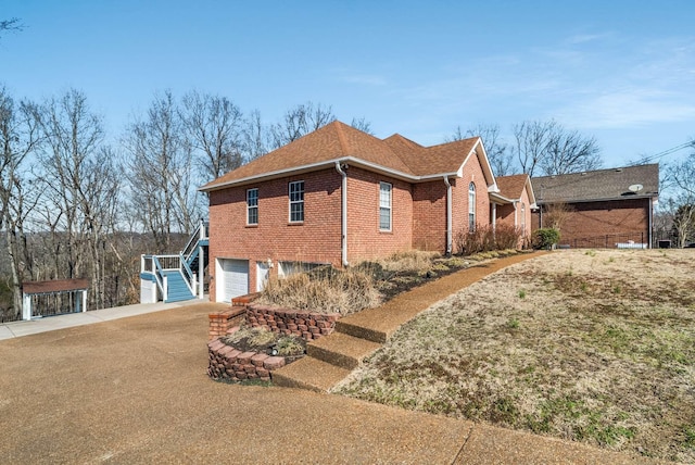 view of side of home with driveway, roof with shingles, a garage, and brick siding