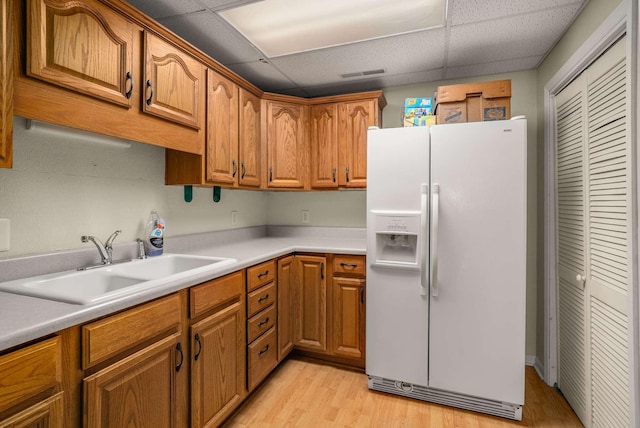 kitchen with white refrigerator with ice dispenser, a sink, visible vents, brown cabinets, and light wood finished floors