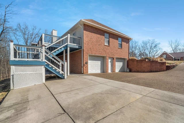 view of home's exterior with concrete driveway, a chimney, stairway, an attached garage, and brick siding