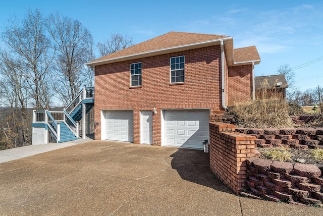 view of home's exterior with brick siding, a shingled roof, stairway, a garage, and driveway