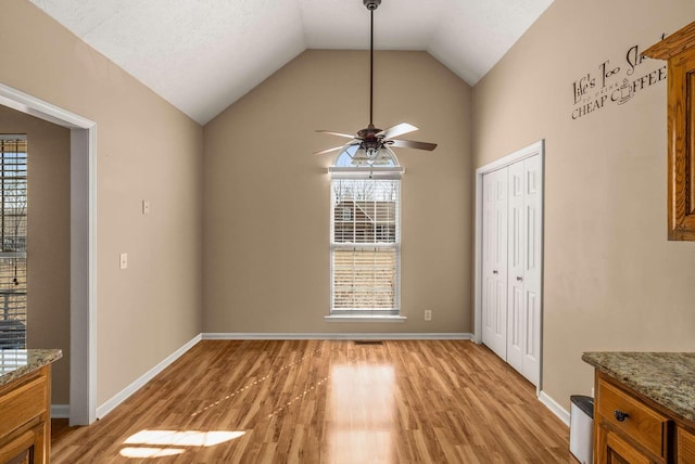 unfurnished dining area featuring lofted ceiling, light wood-style flooring, baseboards, and a ceiling fan