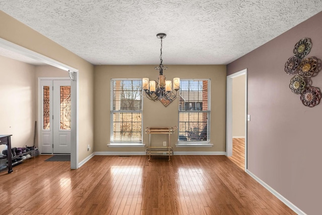 dining area featuring a chandelier, a textured ceiling, wood-type flooring, and baseboards