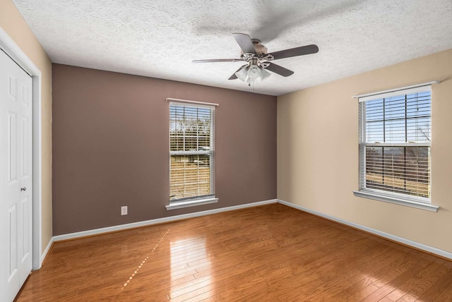 unfurnished room featuring ceiling fan, a textured ceiling, light wood-type flooring, and baseboards