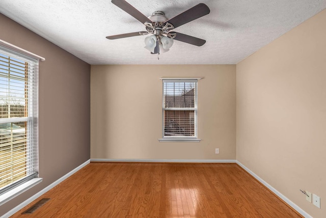 empty room featuring baseboards, a textured ceiling, visible vents, and wood finished floors