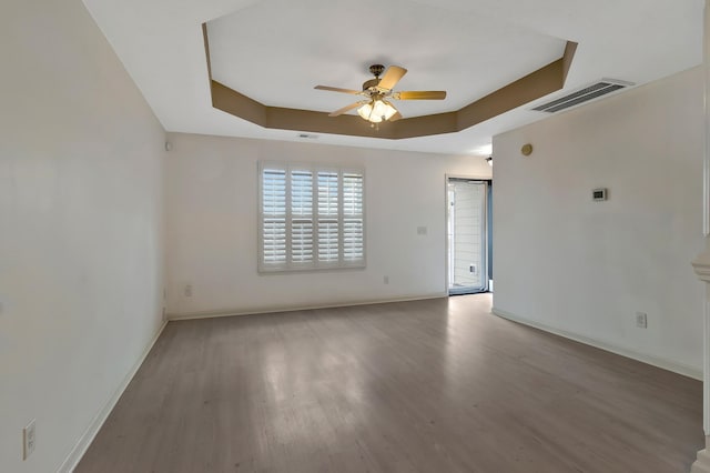 empty room featuring wood finished floors, visible vents, baseboards, a ceiling fan, and a raised ceiling