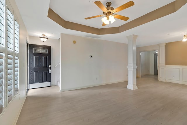 entryway with ceiling fan, light wood finished floors, a raised ceiling, and ornate columns