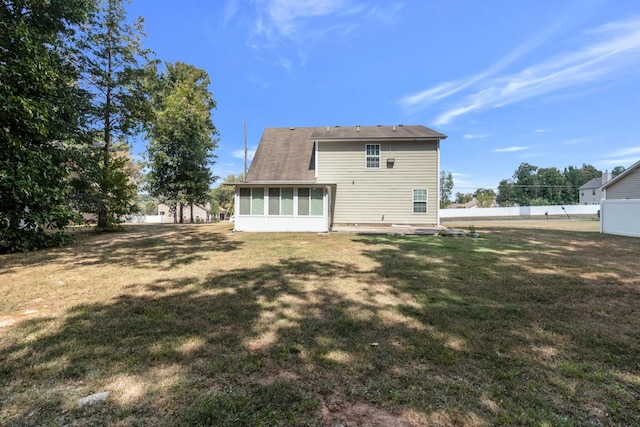 rear view of house featuring a sunroom, fence, and a lawn