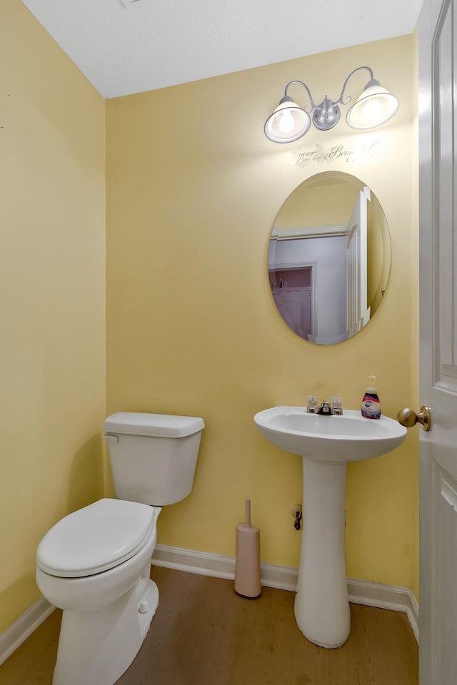 bathroom with toilet, a sink, baseboards, and wood finished floors