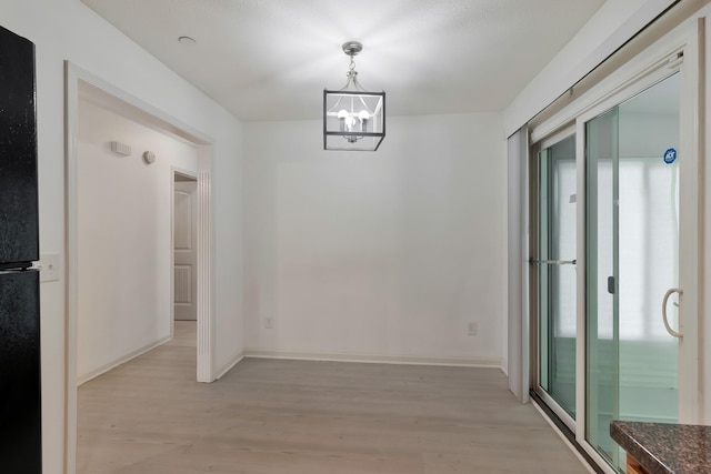 unfurnished dining area with a chandelier, light wood-type flooring, and baseboards