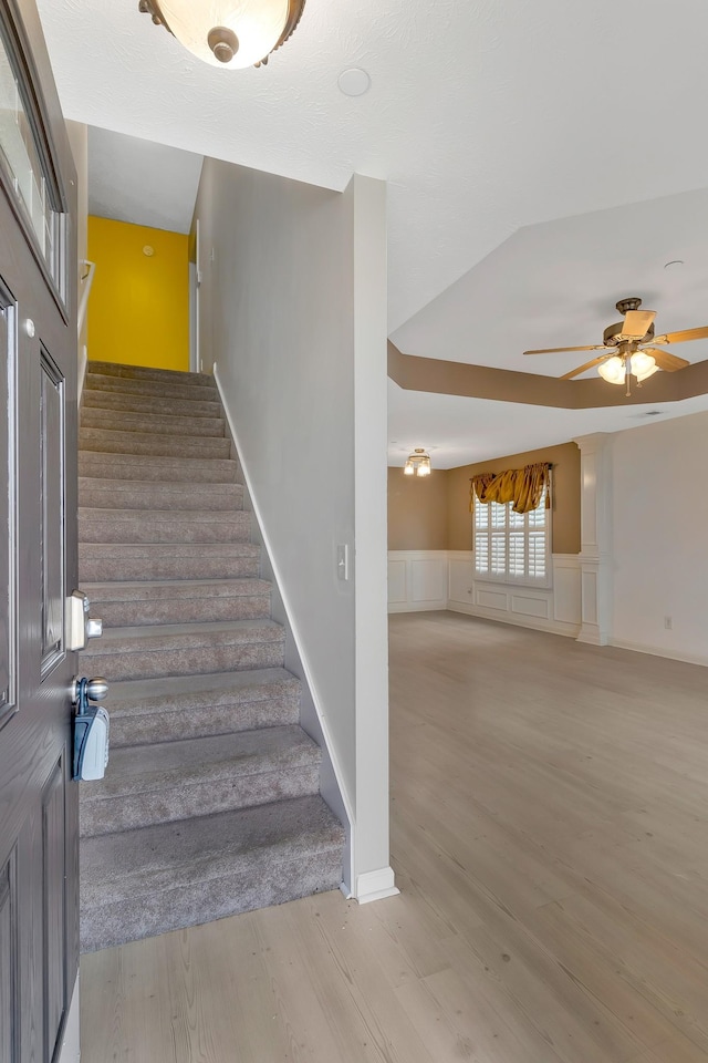 stairway with a ceiling fan, wainscoting, a decorative wall, and wood finished floors