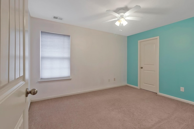 empty room featuring ceiling fan, visible vents, baseboards, and light colored carpet