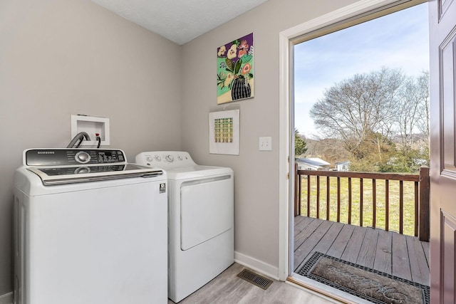 clothes washing area with laundry area, visible vents, baseboards, light wood-style floors, and washing machine and dryer