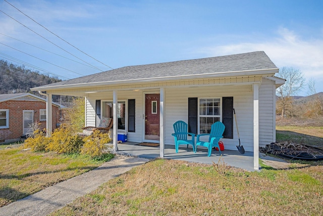 bungalow featuring covered porch, a front lawn, and roof with shingles