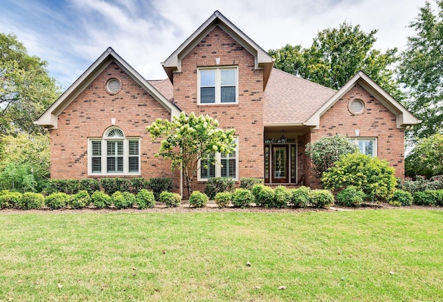 traditional home with roof with shingles, a front lawn, and brick siding