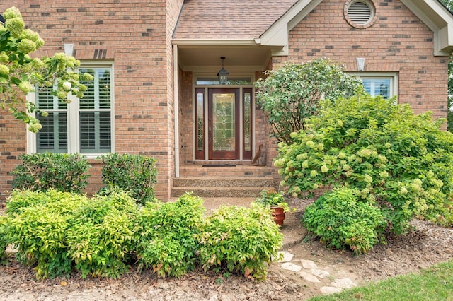 doorway to property featuring a shingled roof and brick siding