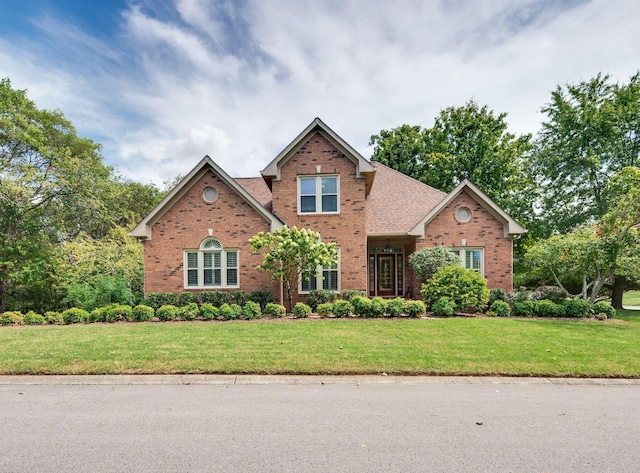 traditional-style home featuring roof with shingles, a front lawn, and brick siding