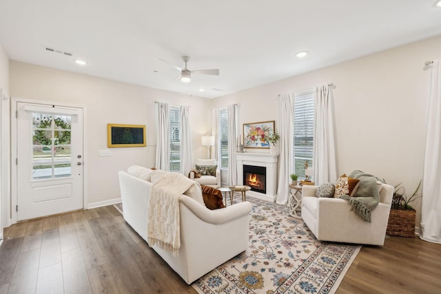 living area with a warm lit fireplace, recessed lighting, wood finished floors, and a healthy amount of sunlight