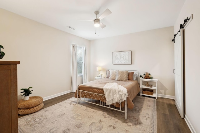 bedroom with a barn door, visible vents, baseboards, ceiling fan, and wood finished floors