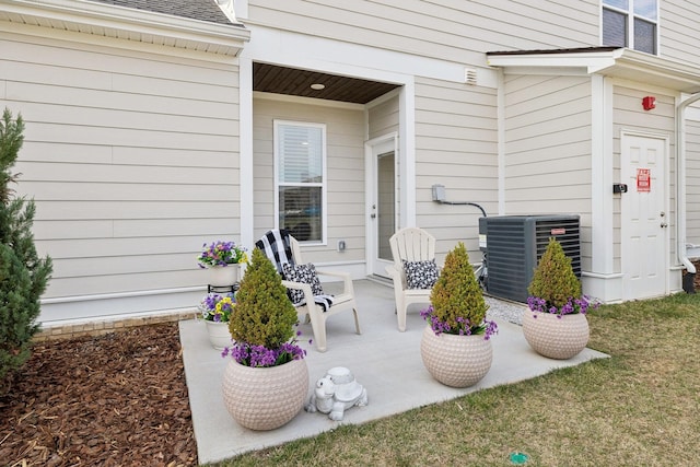 entrance to property featuring a shingled roof, covered porch, and central AC