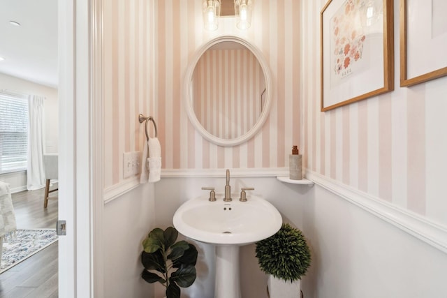 bathroom with wood finished floors, a sink, and wallpapered walls