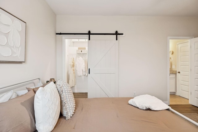 bedroom with ensuite bath, a barn door, and wood finished floors