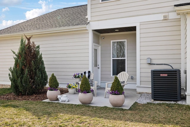 entrance to property featuring a shingled roof, a lawn, and central air condition unit