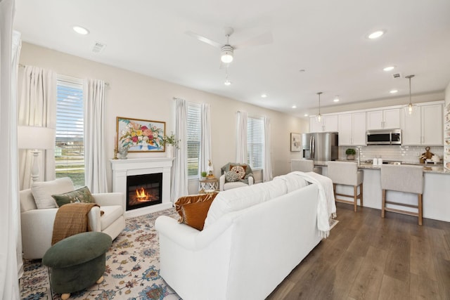 living area featuring ceiling fan, a glass covered fireplace, dark wood finished floors, and recessed lighting