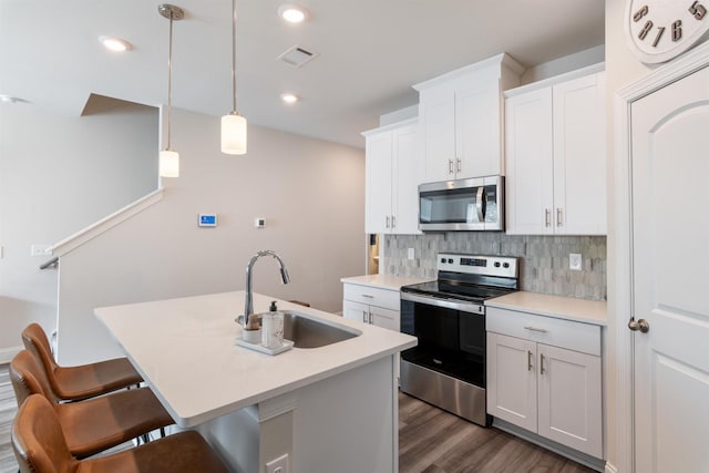 kitchen with visible vents, backsplash, appliances with stainless steel finishes, a kitchen island with sink, and a sink