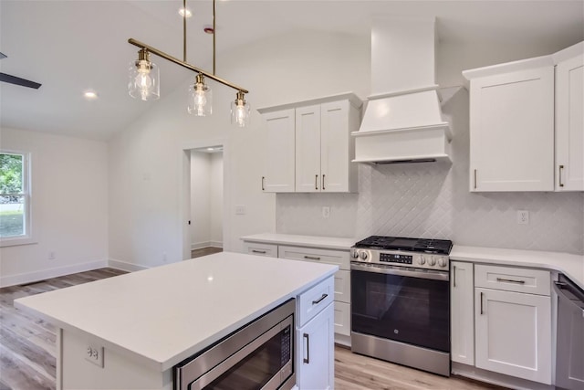 kitchen featuring lofted ceiling, light countertops, appliances with stainless steel finishes, decorative backsplash, and custom range hood