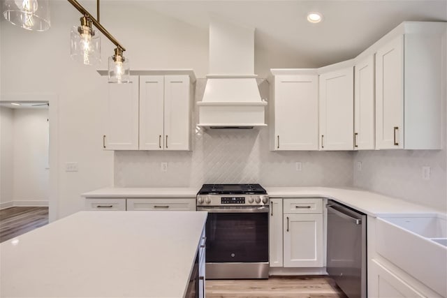 kitchen with premium range hood, white cabinets, light countertops, appliances with stainless steel finishes, and backsplash