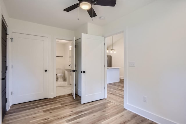 unfurnished bedroom with light wood-type flooring, a ceiling fan, baseboards, and connected bathroom