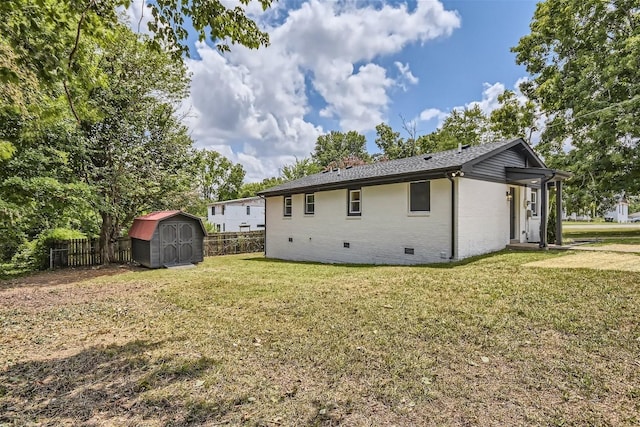 rear view of house featuring an outbuilding, crawl space, a storage unit, fence, and a yard