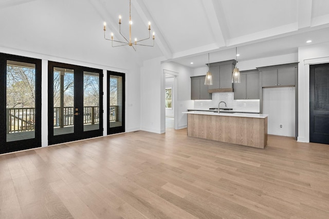 kitchen with a center island with sink, decorative backsplash, gray cabinets, light countertops, and a sink