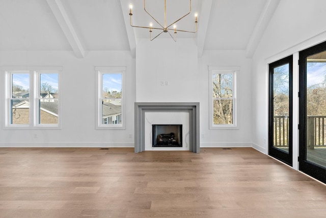 unfurnished living room with lofted ceiling with beams, a premium fireplace, wood finished floors, a chandelier, and baseboards