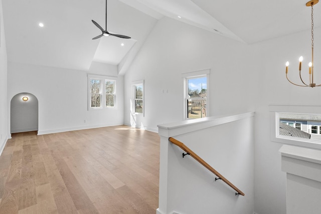 unfurnished living room featuring arched walkways, baseboards, light wood-style flooring, high vaulted ceiling, and ceiling fan with notable chandelier