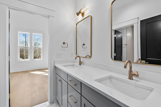 full bathroom with wood finished floors, a sink, baseboards, and double vanity